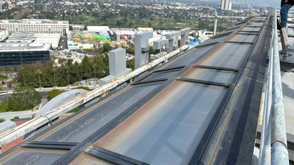 A detailed view of pooled brown water and rusty discoloration gathering along the metal framing and tracks of a commercial glass skylight.