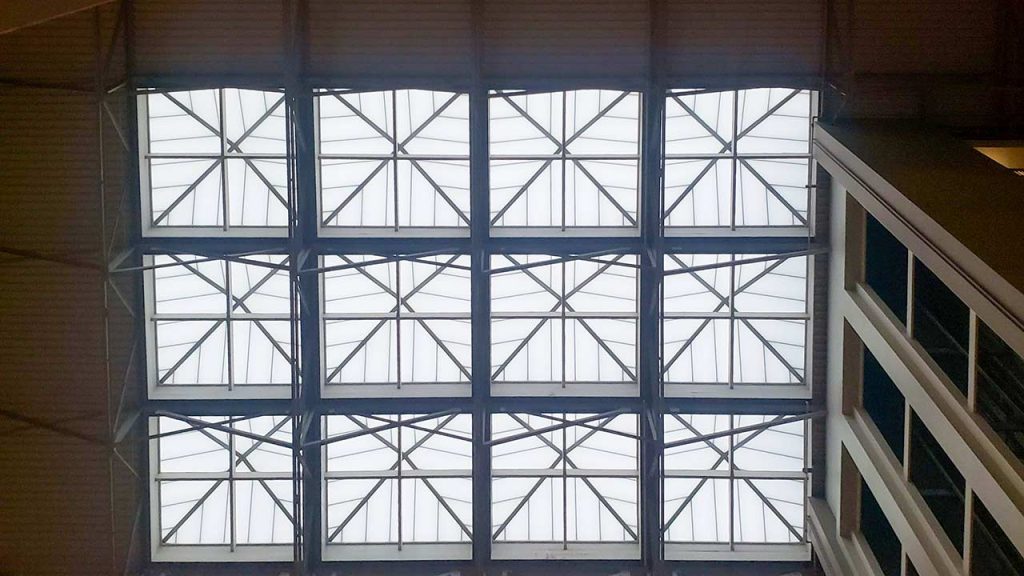 Cluster of twelve, pyramid skylight with geometric grid pattern viewed from below in an indoor setting, emitting soft, diffused light. The tone is calm and structured.