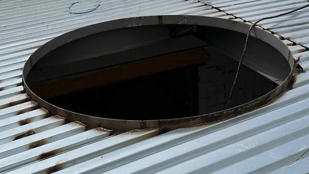 A circular opening cut into a metal roof.
