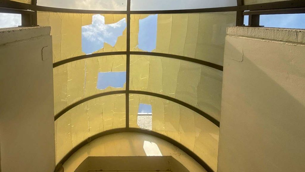 Inside view of a stairwell featuring a yellowed and broken skylight panels.