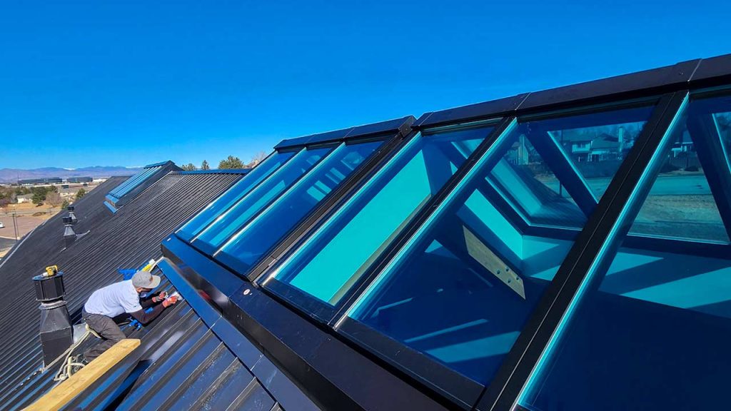 A man is on a roof, focusing on the installation of Velux Modular ridge skylights, with tools nearby.