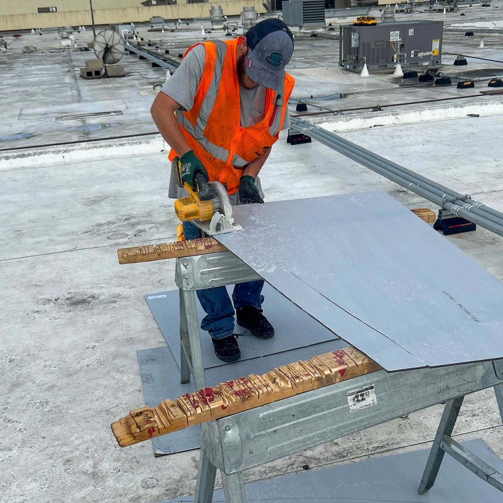 A technician in an orange vest is using a saw to cut a replacement panel.