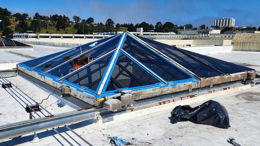 The pyramid glass skylight has sections masked with tape to allow the application of a silicone sealant.
