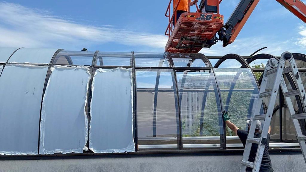 Technicians on a manlift and on the roof work on installing polycarbonate sheets on a barrel vault skylight.
