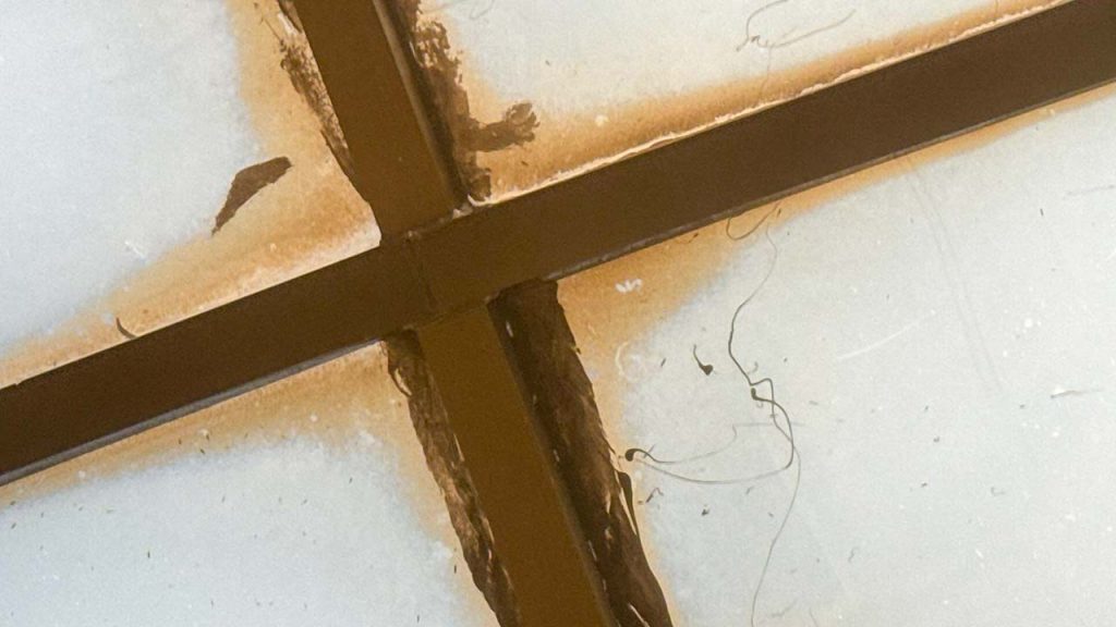 Q closeup view of rusty looking deposits and sloppi;ly applied caulking material seen from the interior.