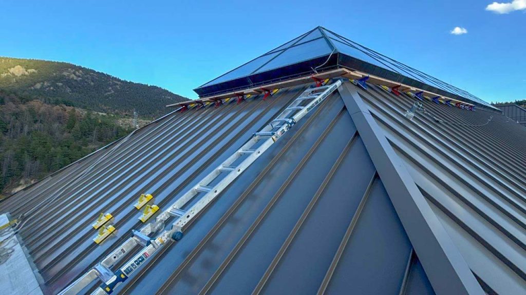 A ladder mounted on the metal roof leads to a wooden catwalk surrounding the skylight at the top.