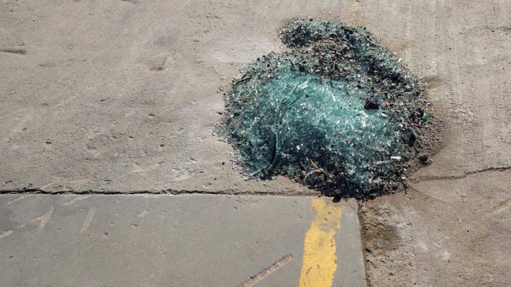A pile of shattered glass lies on a rough concrete surface with a faded yellow line nearby, conveying a sense of disorder and neglect.