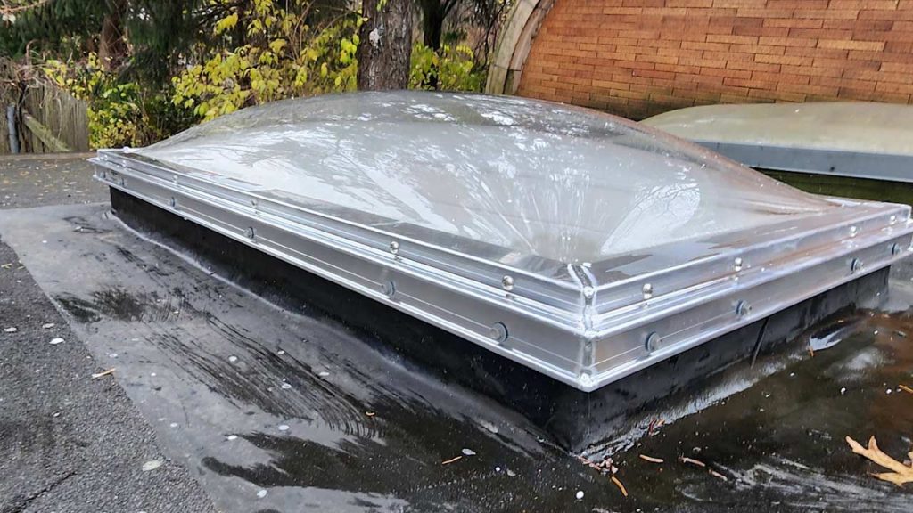 A dome-shaped skylight on a flat roof after a fire. The surrounding area is charred, with autumn leaves nearby, creating a somber mood.