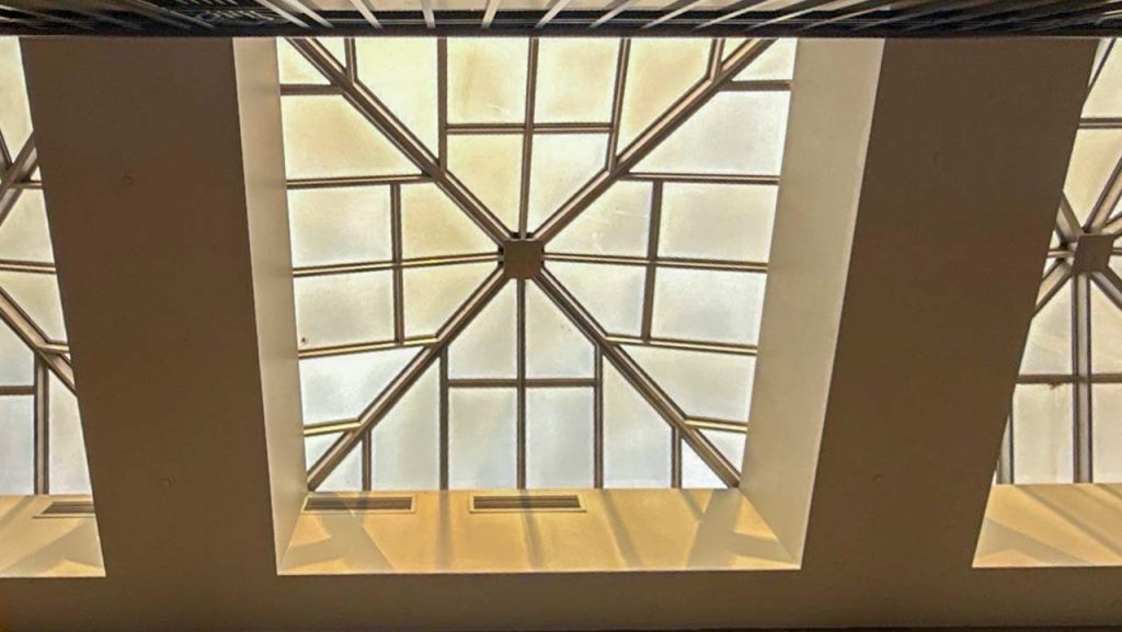 Ceiling view showing a geometric skylight with a grid-like pattern. Sunlight filters through, creating a warm, serene ambiance.