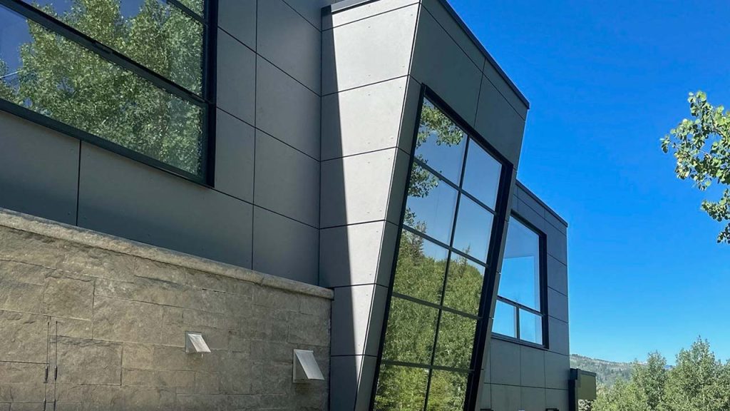 Modern building with angular, geometric lines and large windows against a clear blue sky. Trees reflect on the glass, creating a serene atmosphere.