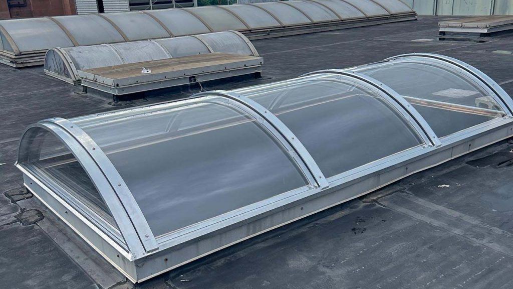 A rooftop features several translucent, barrel vault skylights lined in metal. The scene is industrial with a modern, utilitarian feel. Dark roof surface.