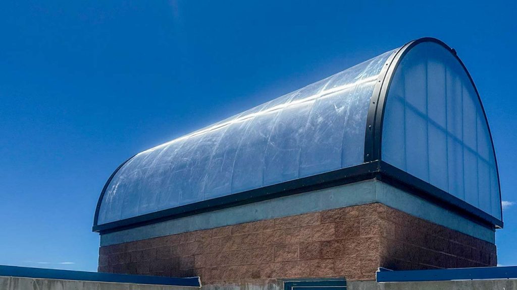 A barrel vault skylight with translucent panels sits atop a brick structure against a clear blue sky. The scene conveys a sense of tranquility.