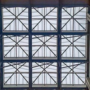 Ceiling grid of nine square pyramid skylights with geometric patterns as seen feom below. The structure's metal frames and frosted glass panels create a modern, symmetrical design.
