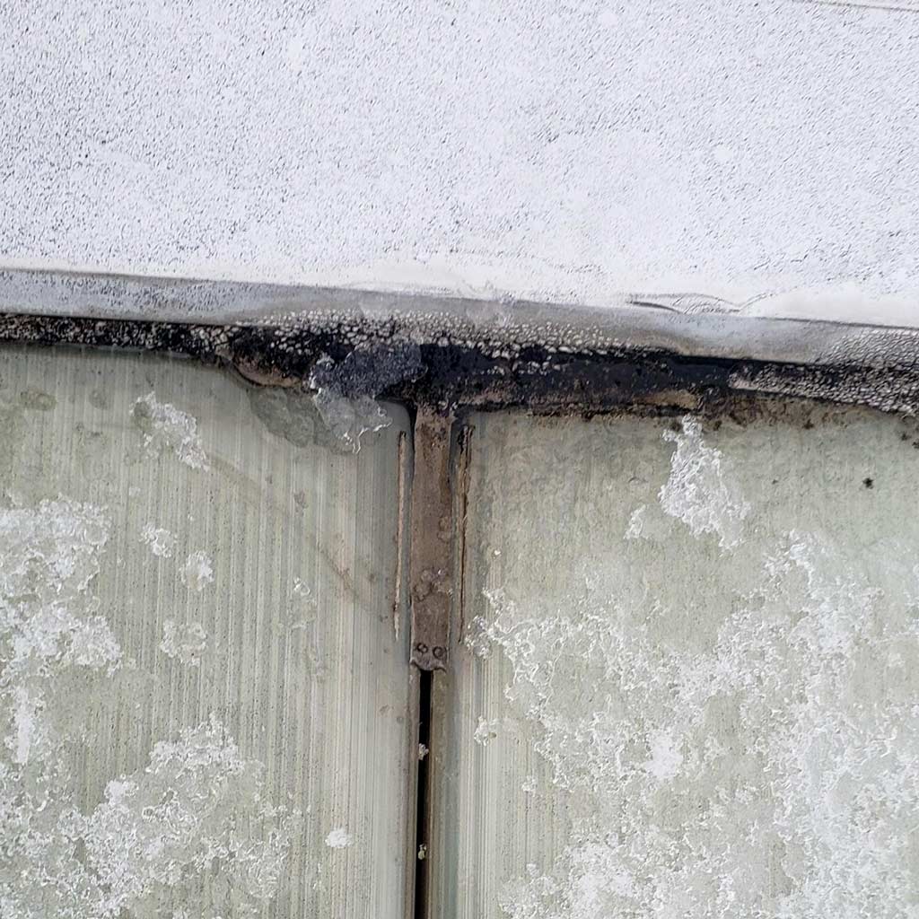 Close-up of a frosted, snow-covered skylight frame and another leark source with dark mold or dirt along the edge, highlighting weather damage and decay.