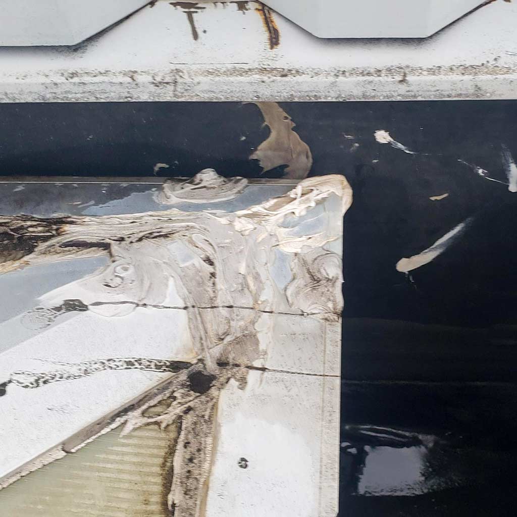 Close-up of a skylight corner with peeling caulking and patches of dark and light areas. The texture suggests weathering and decay, evoking neglect.