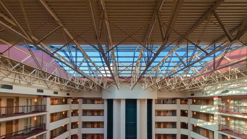 View of an atrium in a multi-story building with balconies on each floor. The ceiling features a geometric glass skylight letting in natural light.