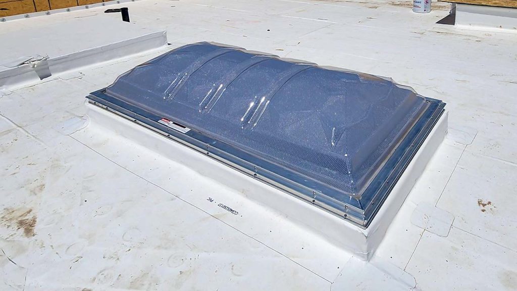 A clear, domed skylight on a flat white rooftop, reflecting sunlight. The scene is bright, suggesting a sunny and clear day, conveying openness and modernity.