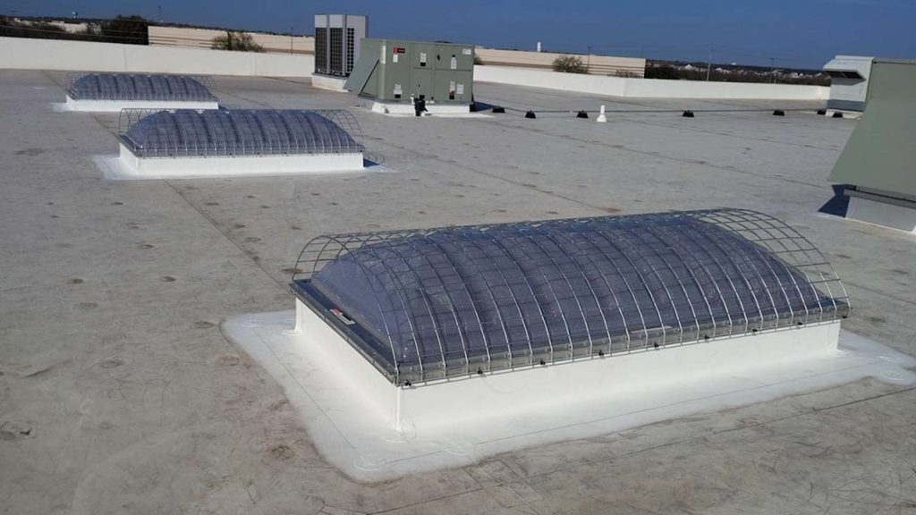A flat rooftop with four arched skylights covered by exterior safety screens. The roof is light-colored, with an HVAC unit visible in the background.