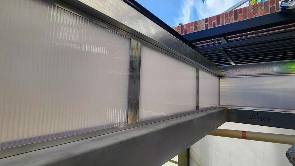 View of a metal and translucent wall panels structure extending towards a partially visible sky. The scene conveys an industrial and modern tone.