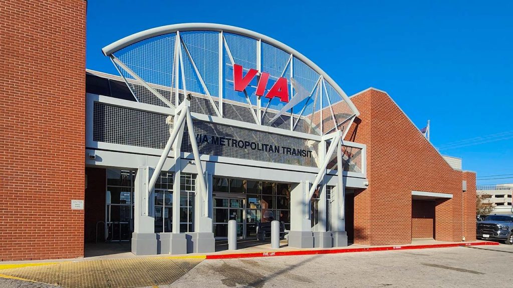 Exterior of VIA Metropolitan Transit building with a modern design, brick walls, and a large arched sign. Clear blue sky in the background.