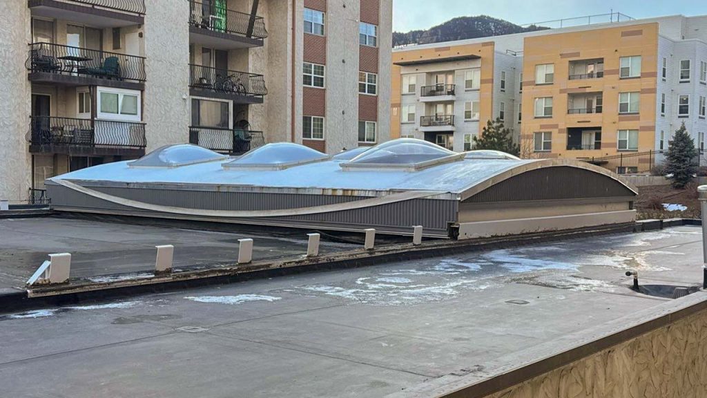 Unique building in an urban area with a UFO-shaped retractable roof featuring four large domes. Surrounded by modern apartments, setting a futuristic tone.