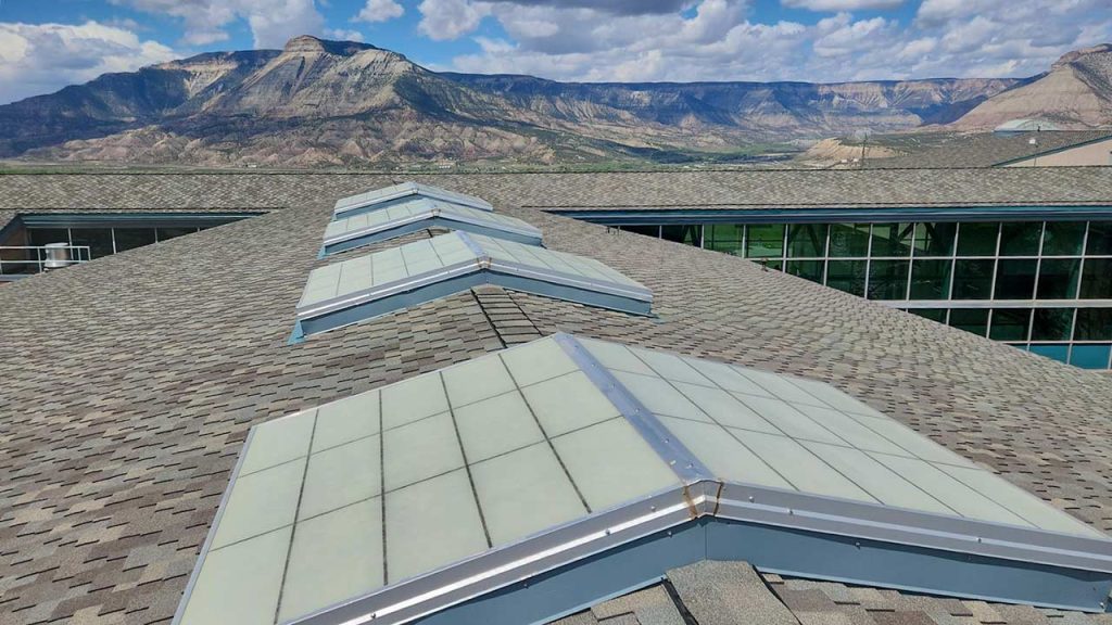A rooftop with multiple skylights set against a backdrop of rugged mountains. The sky is partly cloudy, and the mood is serene and expansive.