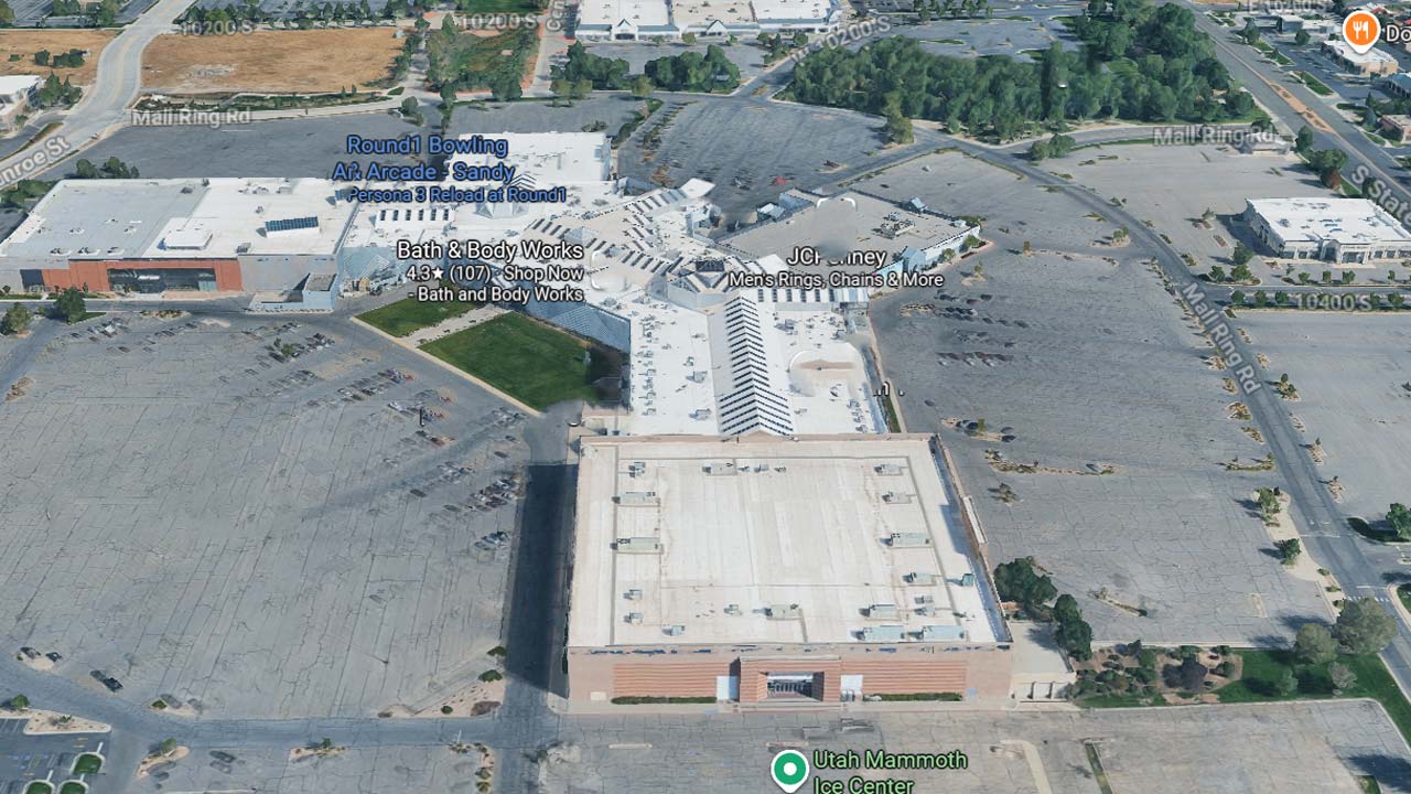 Aerial view of a shopping mall with large adjacent parking lots, a few parked cars, and surrounding green areas. Notable stores are labeled, such as Bath & Body Works and JCPenney.