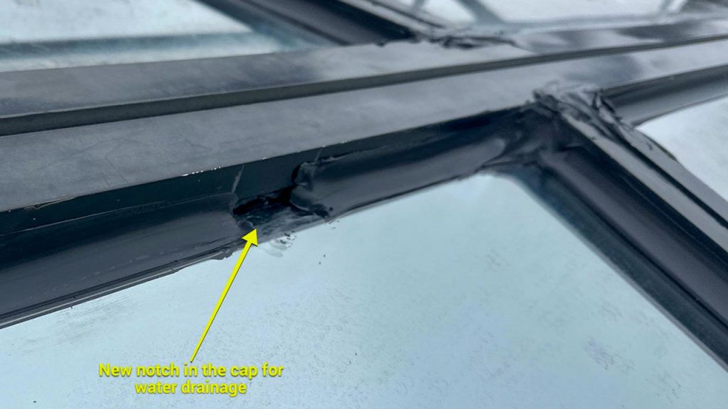 Close-up of a skylight showing a new notch in the black cap for water drainage. The notch allows water to escape, indicated by a yellow arrow and text.