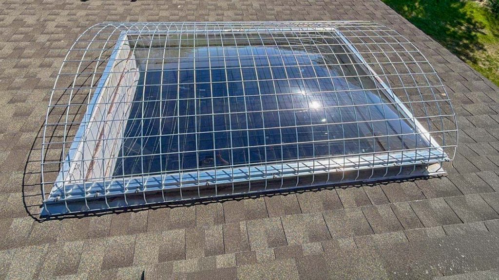 Large polycarbonate dome skylight mounted on an asphalt-shingled roof with a protective metal security cage at Louisville Golf Course pumphouse.