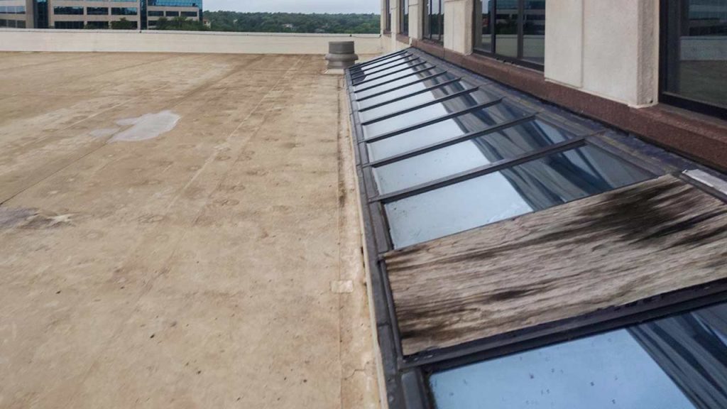 Commercial single-slope glass skylight with temporary plywood panel repair on hotel roof