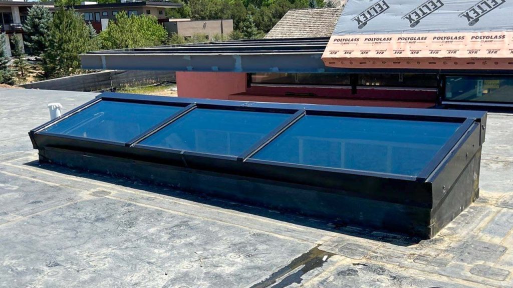Angled single-pitch glass skylight with aluminum framing mounted on a raised curb along a commercial rooftop.