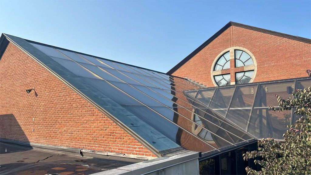 Large sloped glass commercial skylight structure installed along a brick building wall at Corpus Christi Church**