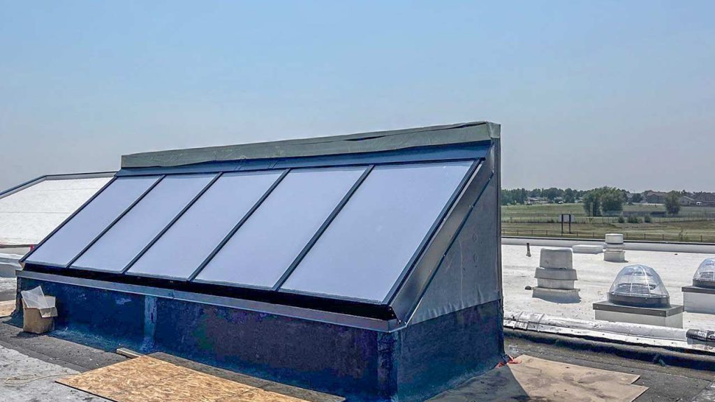 Large commercial skylight structure installed on a building roof under a clear blue sky.