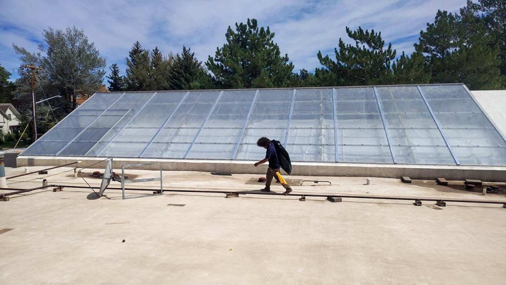 Technician walking along a large commercial sloped skylight during wet seal repair at Ace Hardware in Laramie