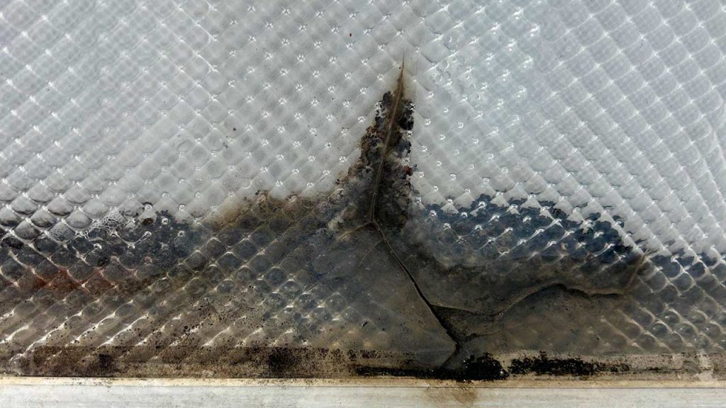 Severe crack and dirt buildup on a textured prismatic skylight dome before replacement